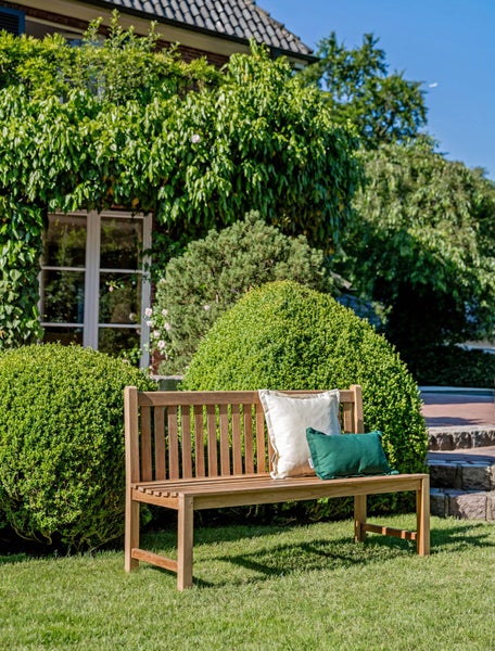 Holzgartenbank mit Kissen auf Rasen vor einem Haus
