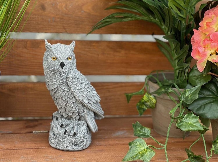 Dekorative Eulenfigur aus Kunststein zur Gartendekoration auf einem Holzuntergrund.