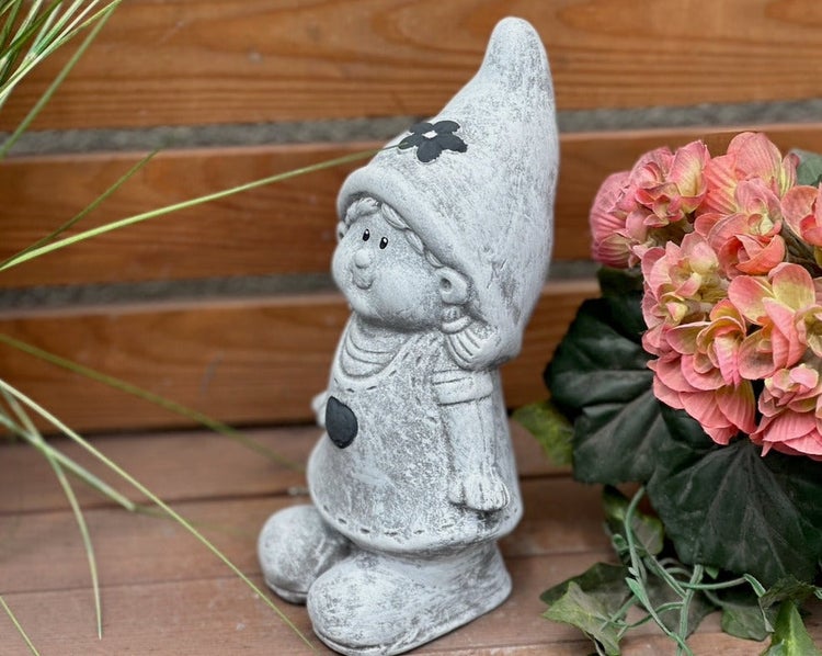 Gartenfigur Wichtelmädchen aus grauem Steinguss mit Zipfelmütze auf einer Holzfläche stehend.