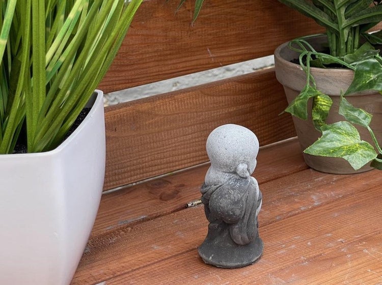 Kleine dekorative Buddha Figur aus Stein für den Garten auf einer Holzoberfläche zwischen Topfpflanzen.