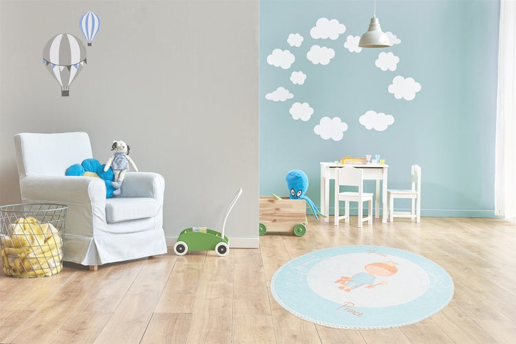 Helles Kinderzimmer mit Holzboden, rundem Kinderteppich mit Prinzen-Motiv, Kindersitzgruppe, Wandtattoos mit Wolken und Heißluftballons sowie Sessel.