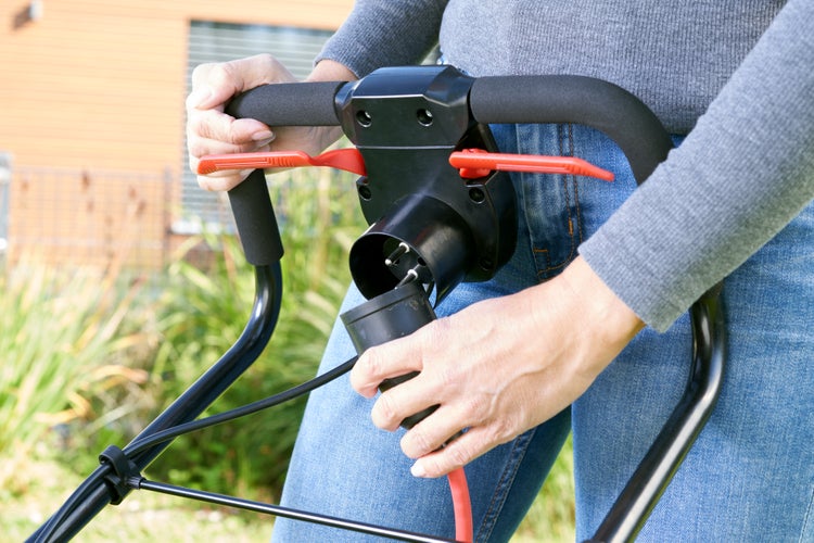 Person steckt Netzkabel in Elektro Rasenmäher Schaltereinheit