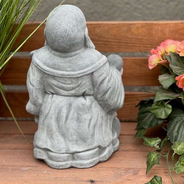 Rückansicht einer Buddha Gartenfigur aus Stein auf einer Holzunterlage mit Pflanzen im Hintergrund
