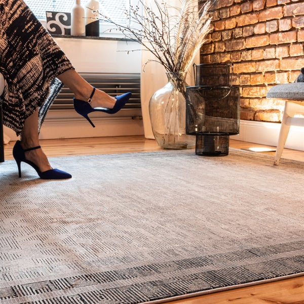 Moderner Teppich mit geometrischem Muster in einem Wohnzimmer mit Backsteinwand, Holzfußboden und dekorativen Elementen.