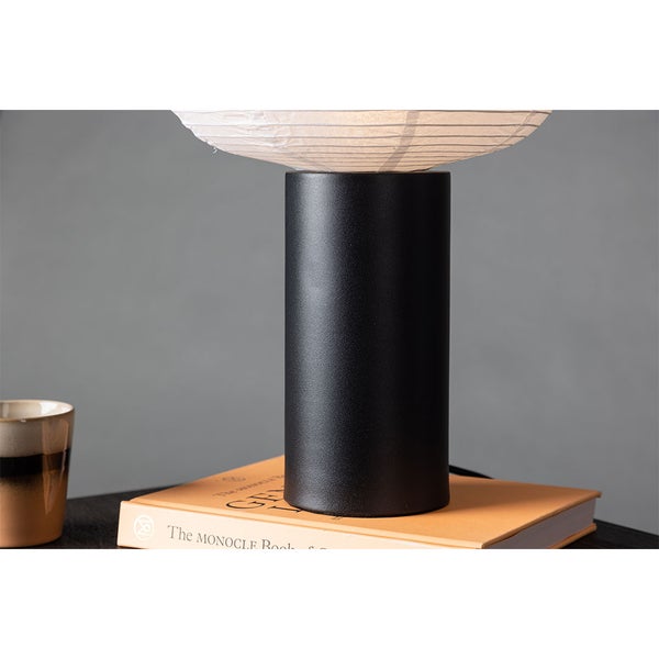 Tischleuchte mit Papierschirm auf einem Nachttisch mit Buch und Tasse