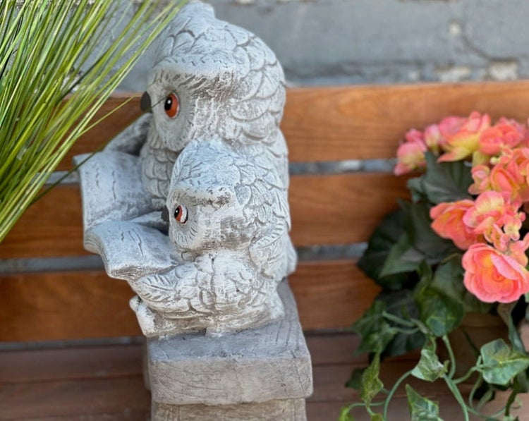 Gartenfigur aus Stein in Form von zwei lesenden Eulen auf einer Holzbank.