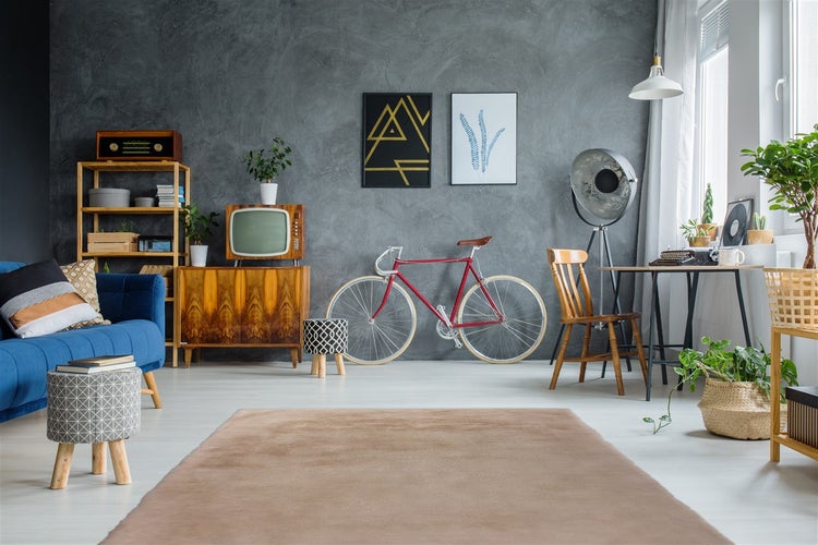 Wohnzimmer im Vintage-Stil mit grauer Strukturwand, blauem Sofa, rotem Fahrrad, Holzmöbeln, beigem Teppich und Zimmerpflanzen.