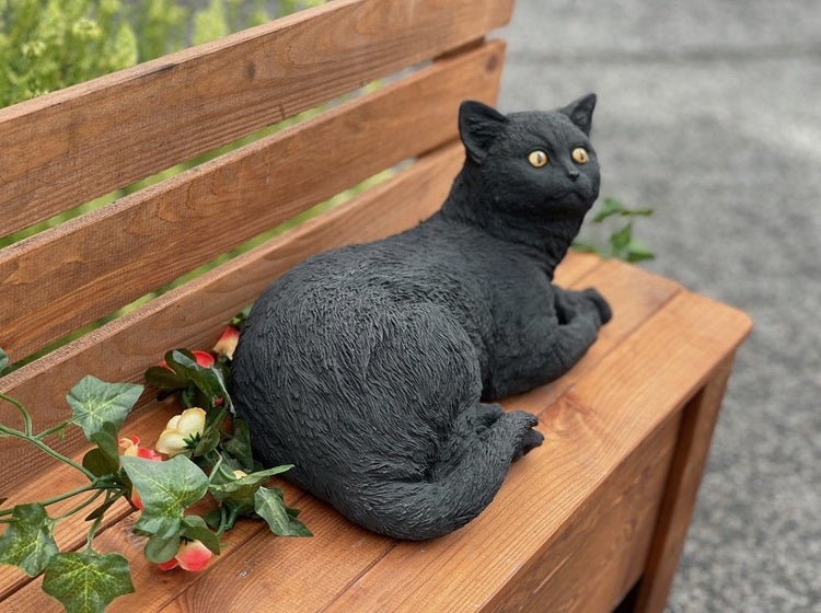Dekorative Gartenfigur Katze aus Kunststein liegend auf einer Holzbank mit Efeu.
