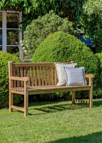 Gartenszene mit Holzbank, Kissen, Tasche und bepflanzten Blumentöpfen.