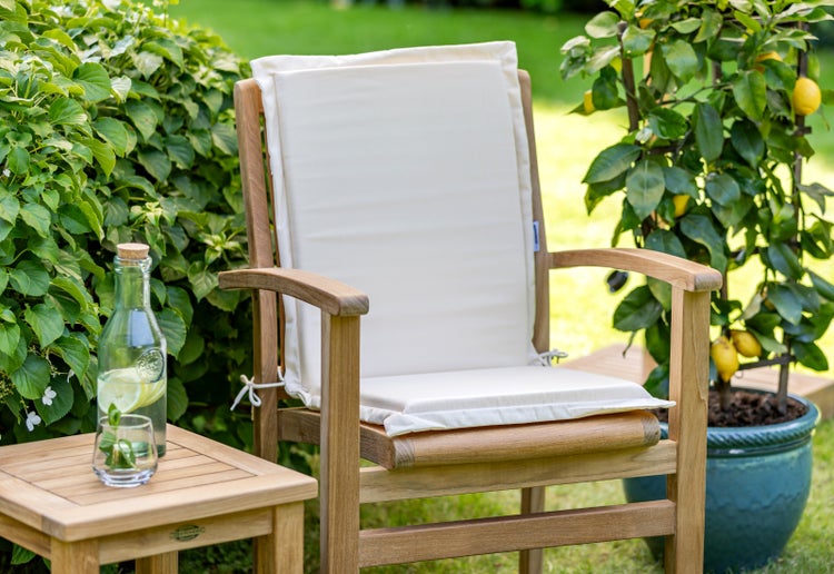 Gartenszene mit einem Holzstuhl und Sitzkissen, einem Beistelltisch mit Getränken und einer Zitronenpflanze