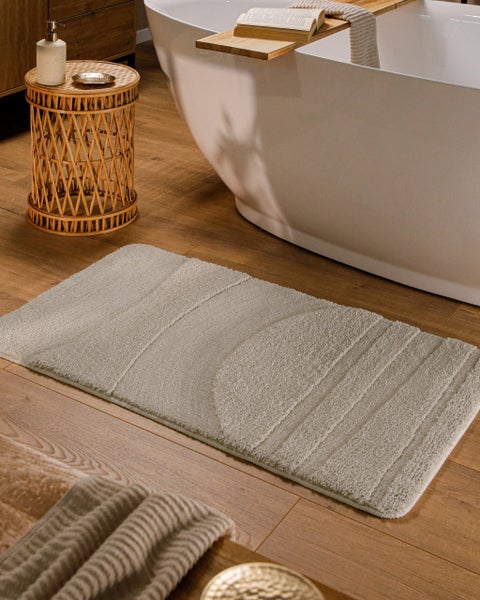Rechteckiger Badteppich mit strukturiertem Muster aus Halbkreis und Streifen auf einem Holzfußboden neben einer freistehenden Badewanne.