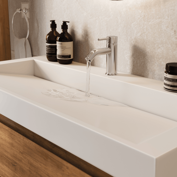 Modernes, rechteckiges Mineralguss-Waschbecken mit fließendem Wasser aus einer Chrom-Einhebelarmatur auf einem Holz-Waschtisch.