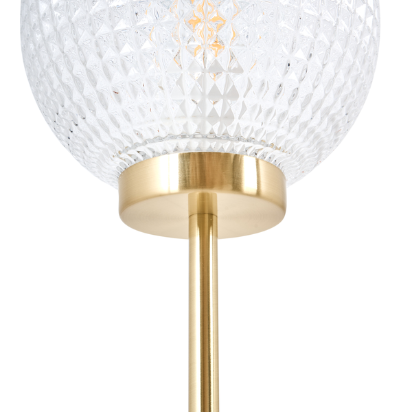 Detailansicht einer Stehlampe mit einem klaren, facettierten Glasschirm und einem goldenen Metallfuß
