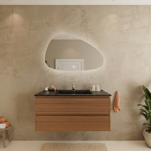 Modernes Badezimmer mit hängendem Waschtischunterschrank in Holzoptik, schwarzem Waschbecken und einem asymmetrischen LED Spiegel.