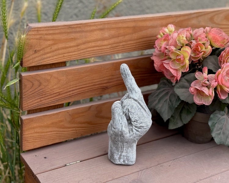 Dekorative Gartenfigur in Form einer Hand mit erhobenem Zeigefinger aus Beton auf einer Holzbank.
