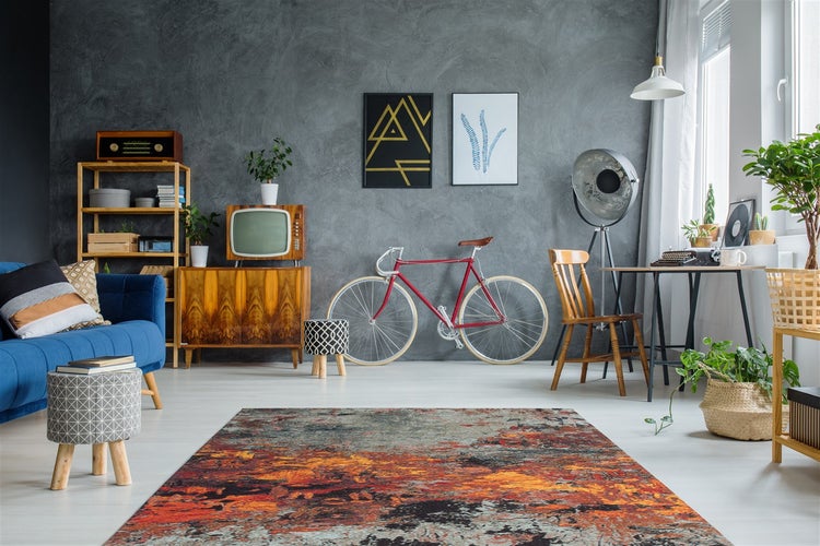 Modernes Wohnzimmer mit bunt gemustertem Teppich, grauer Wand in Betonoptik, Vintage-Möbeln, Retro-Fernseher und einem roten Rennrad.