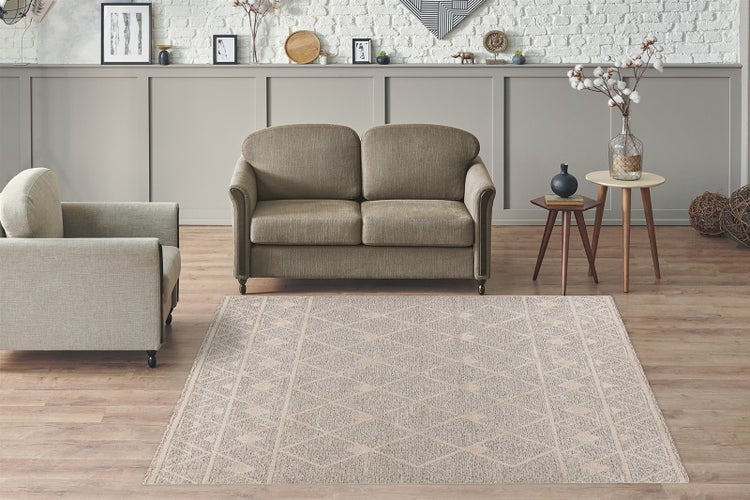 Rechteckiger Teppich mit geometrischem Rautenmuster auf Holzboden in einem hellen Wohnzimmer mit Sofa, Sessel und Beistelltischen.