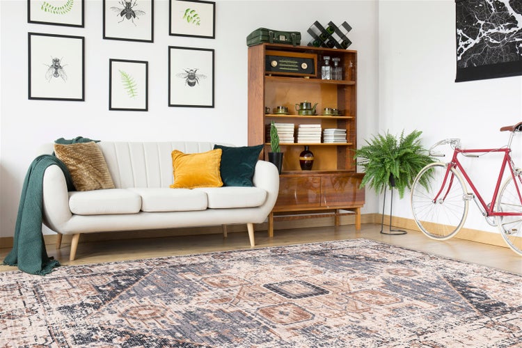 Wohnzimmer mit hellem Sofa, Holzregal, rotem Fahrrad und einem großflächigen Teppich mit orientalischem Muster im Vintage Design.