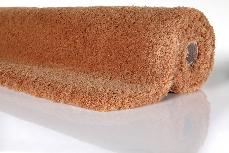 Hellbrauner Hochflorteppich oder Badematte, aufgerollt, weiche Textur.