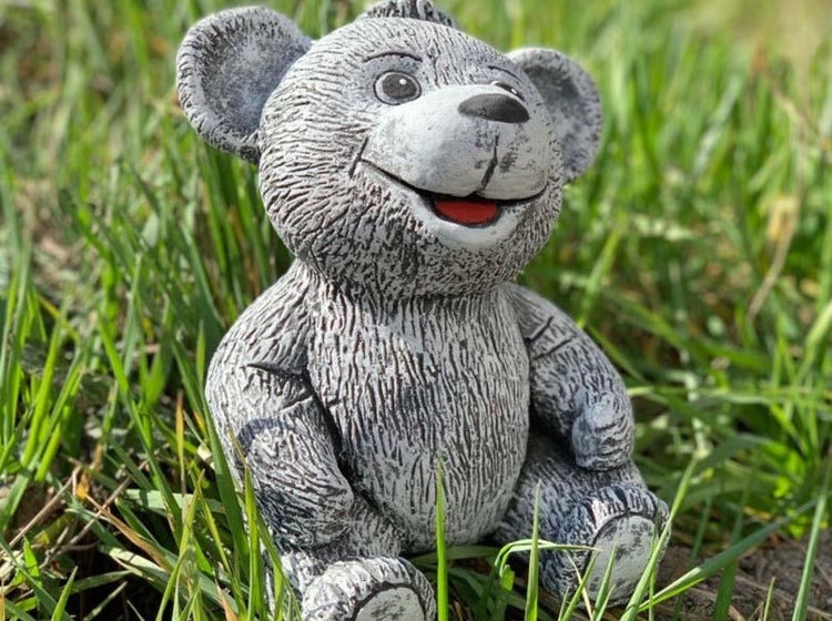 Eine dekorative Gartenfigur in Form eines sitzenden Bären aus Stein im Gras.