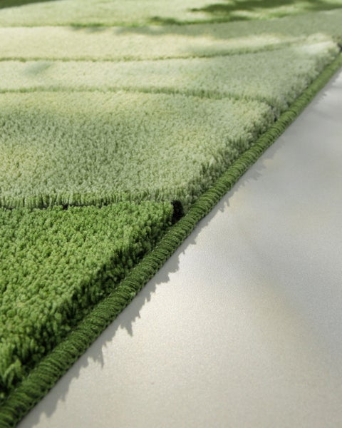 Detailaufnahme eines grünen Teppichs mit Kurzflor und strukturiertem Muster sowie einer umkettelten Kante.