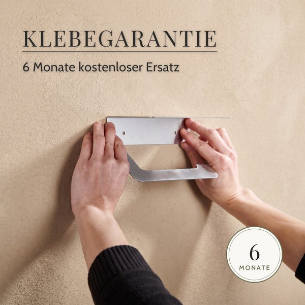 Hände beim Anbringen eines Metall Toilettenpapierhalters an einer Wand mit Hinweis auf 6 Monate Klebegarantie für kostenlosen Ersatz
