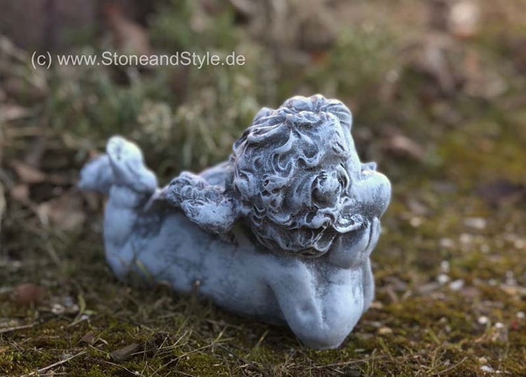 Gartenfigur in Form eines liegenden Engels aus Stein auf einer Wiese