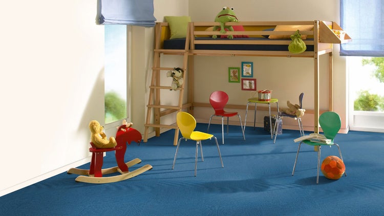 Hell eingerichtetes Kinderzimmer mit blauem Teppichboden, einem Hochbett aus Holz, bunten Stühlen und Spielzeug.