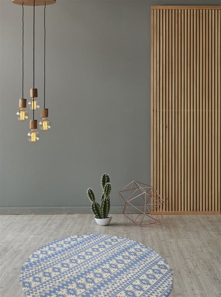 Moderner Wohnraum mit rundem blau-weiß gemustertem Teppich, Holzlamellenwand, Pendelleuchte mit Edison-Glühbirnen, Kaktus und Dekoelement.
