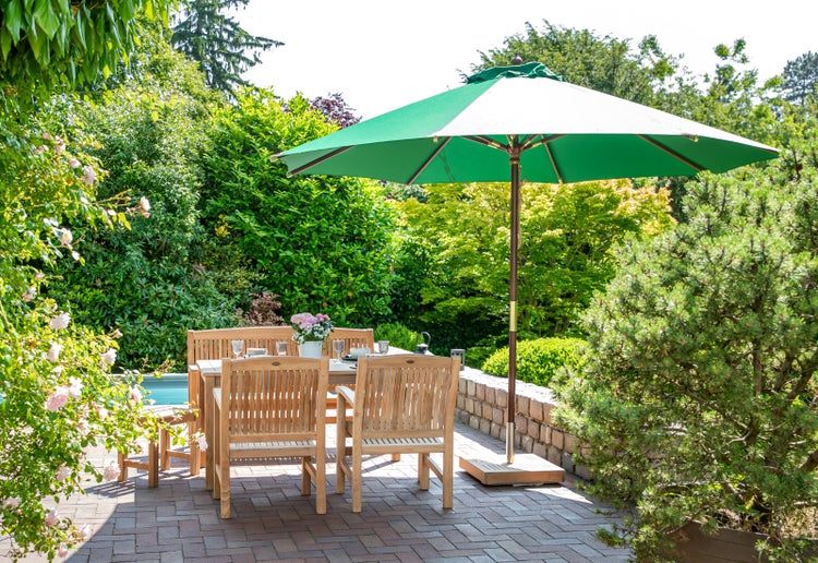 Gartenszene mit Esstischgruppe unter einem Sonnenschirm im Außenbereich.