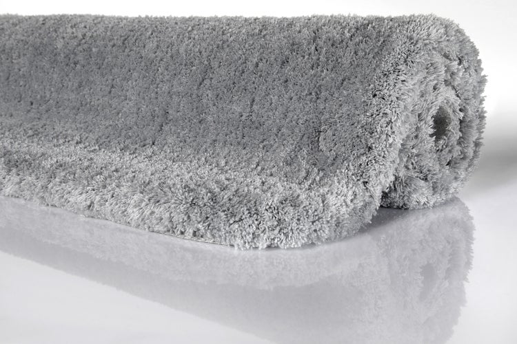 Zusammengerollter grauer Hochflor-Teppich aus weicher Kunstfaser.