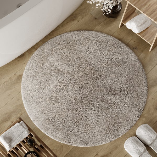 Runder Badeteppich aus Textil auf einem Holzboden in einem hellen, organisierten Badezimmer neben einer Badewanne und Badzubehör aus Holz.