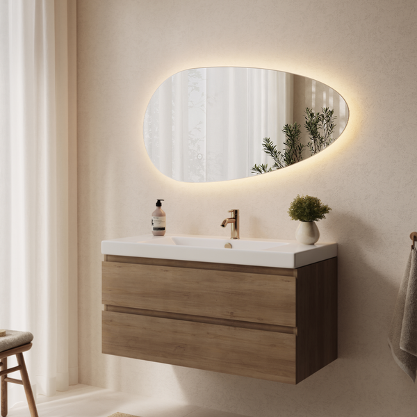 Modernes Badezimmer mit Waschtischunterschrank in Holzoptik, weißem Waschbecken, goldfarbener Armatur und asymmetrischem LED Wandspiegel.
