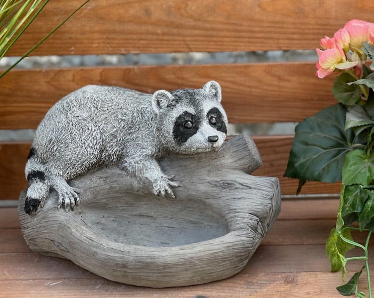 Gartendekoration Waschbär auf einem Baumstamm, der als Vogeltränke oder Pflanzschale dient.