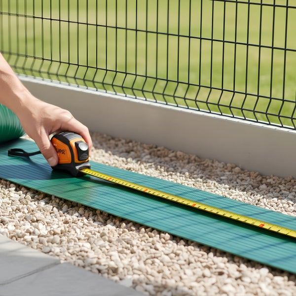 Person misst grüne Rasenkante mit einem Rollbandmaß