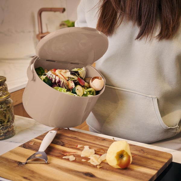 Eine Person wirft Salat in einen Komposteimer in der Küche.