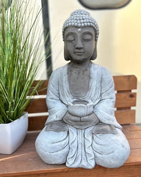 Sitzende Buddha-Gartenfigur in Steinoptik mit einer kleinen Schale in den Händen auf einer Holzbank.