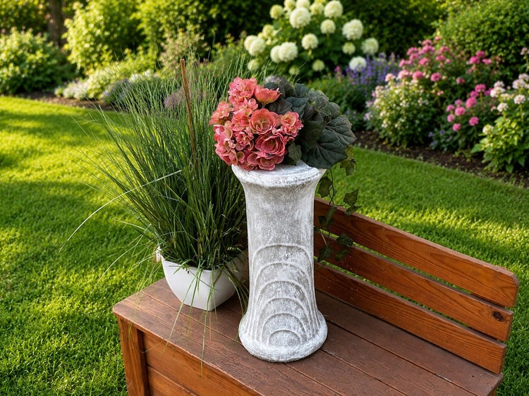 Dekorative Pflanzsäule in Steinoptik mit Begonie auf einer Gartenbank in einem blühenden Garten