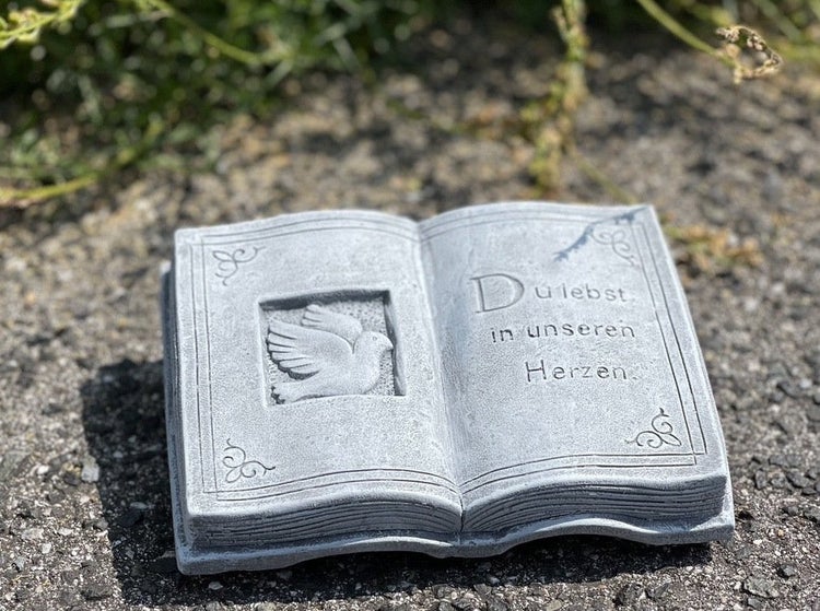 Grabschmuck in Form eines aufgeschlagenen Buches mit Taubenrelief und Inschrift Du lebst in unseren Herzen aus Stein