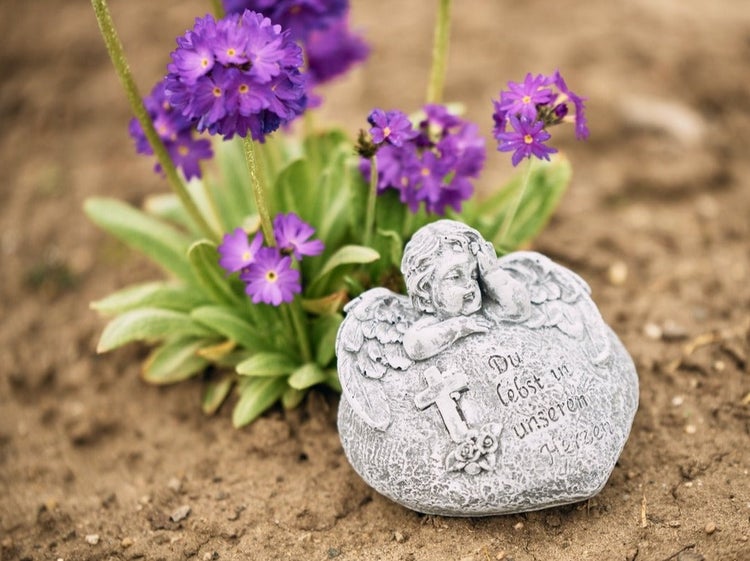 Grabstein aus Stein mit Engel und Gravur Du lebst in unseren Herzen auf Erdboden neben violetten Blumen