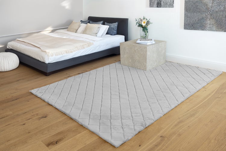 Moderner, heller Schlafraum mit einem rechteckigen grauen Plüschteppich mit Rautenmuster auf Holzboden neben einem Bett und einem Beistelltisch.