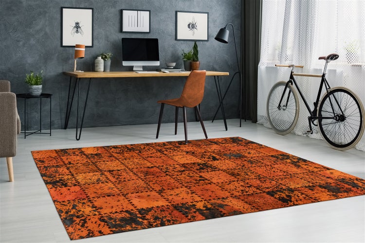 Modernes, organisiertes Arbeitszimmer mit großem Patchwork-Teppich. Holztisch mit Metallbeinen, brauner Stuhl, Fahrrad und minimalistische Wandbilder.