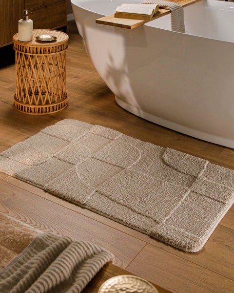 Badematte mit geometrischem Relief-Muster aus Quadraten und Kurven in Beige, weiche Textur.
