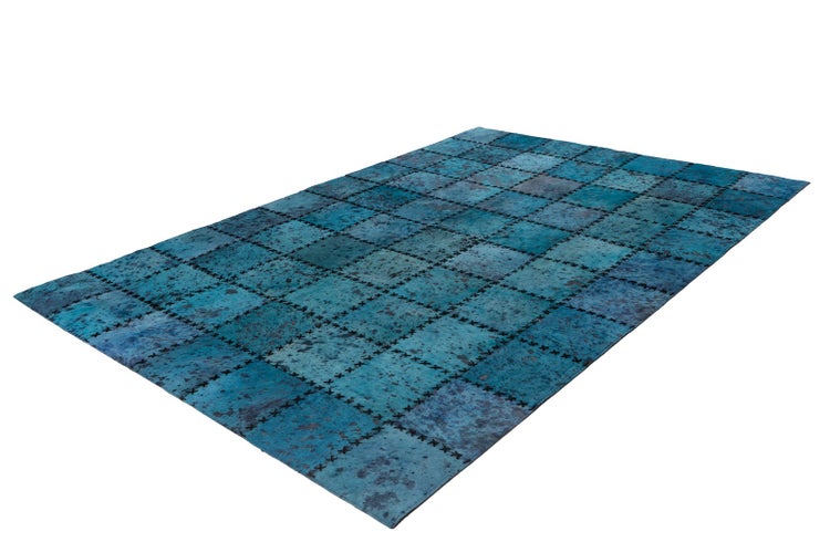 Patchwork-Teppich aus Kuhfell in Blau mit sichtbaren Kreuzstichen zwischen den Quadraten.