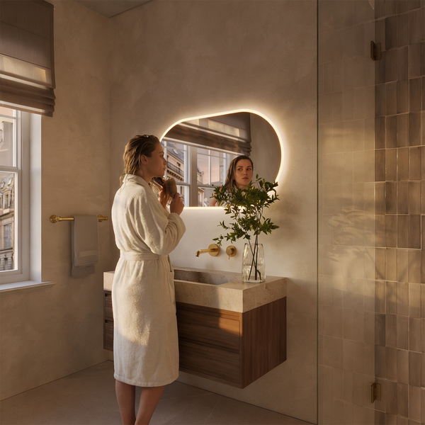 Modernes Badezimmer mit ovalem LED Spiegel, Waschbecken aus Stein auf Holzunterschrank und Armaturen in Metalloptik in einem hellen Badambiente.