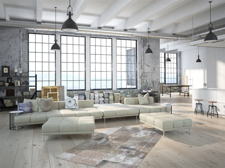 Ein geräumiges, helles Wohnzimmer im Loft-Stil mit großen Fenstern, Betonwänden, einem hellen Ecksofa und industriellen Hängelampen.