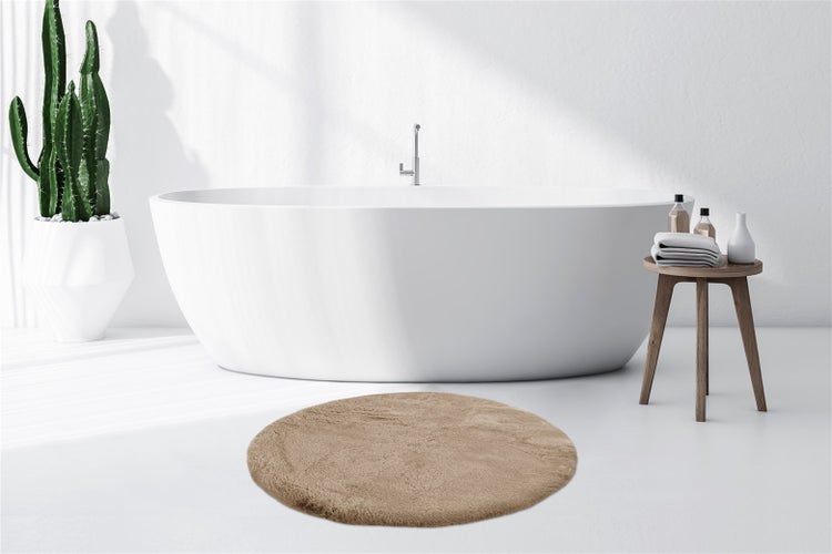 Helles Badezimmer mit freistehender Badewanne, rundem Badeteppich, Kaktus im Pflanzkübel und Holzhocker mit Handtüchern.