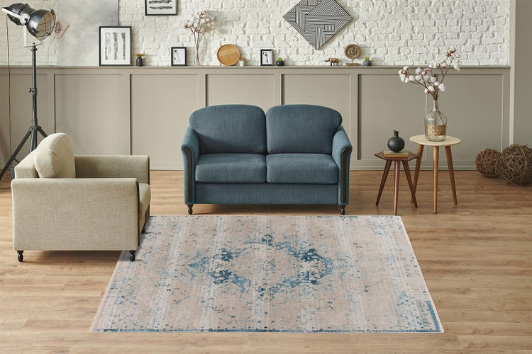 Rechteckiger Teppich mit blau-beigem Vintage-Muster in einem hellen Wohnzimmer mit blauem Sofa, beigem Sessel und Holzboden.