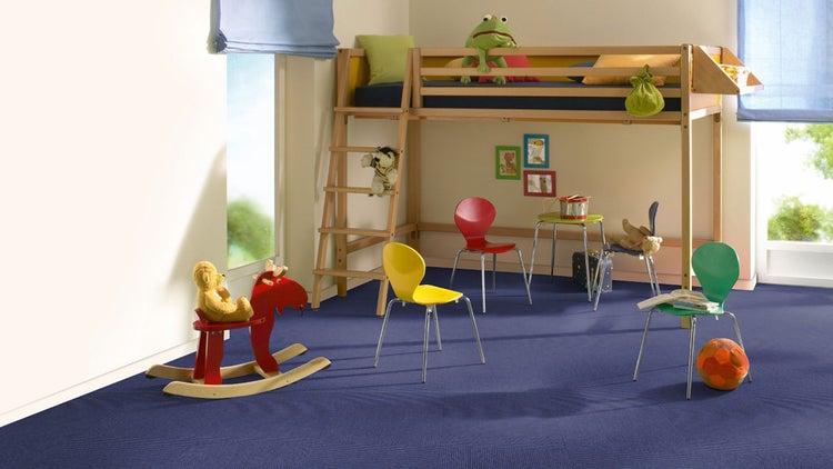 Helles Kinderzimmer mit blauem Teppichboden, Hochbett aus Holz, farbigen Stühlen und einem Schaukelpferd.
