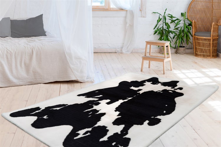 Rechteckiger Teppich mit schwarz-weißem Kuhfellmuster in einem hellen Schlafzimmer mit hellem Holzboden, Himmelbett und Korbsessel.